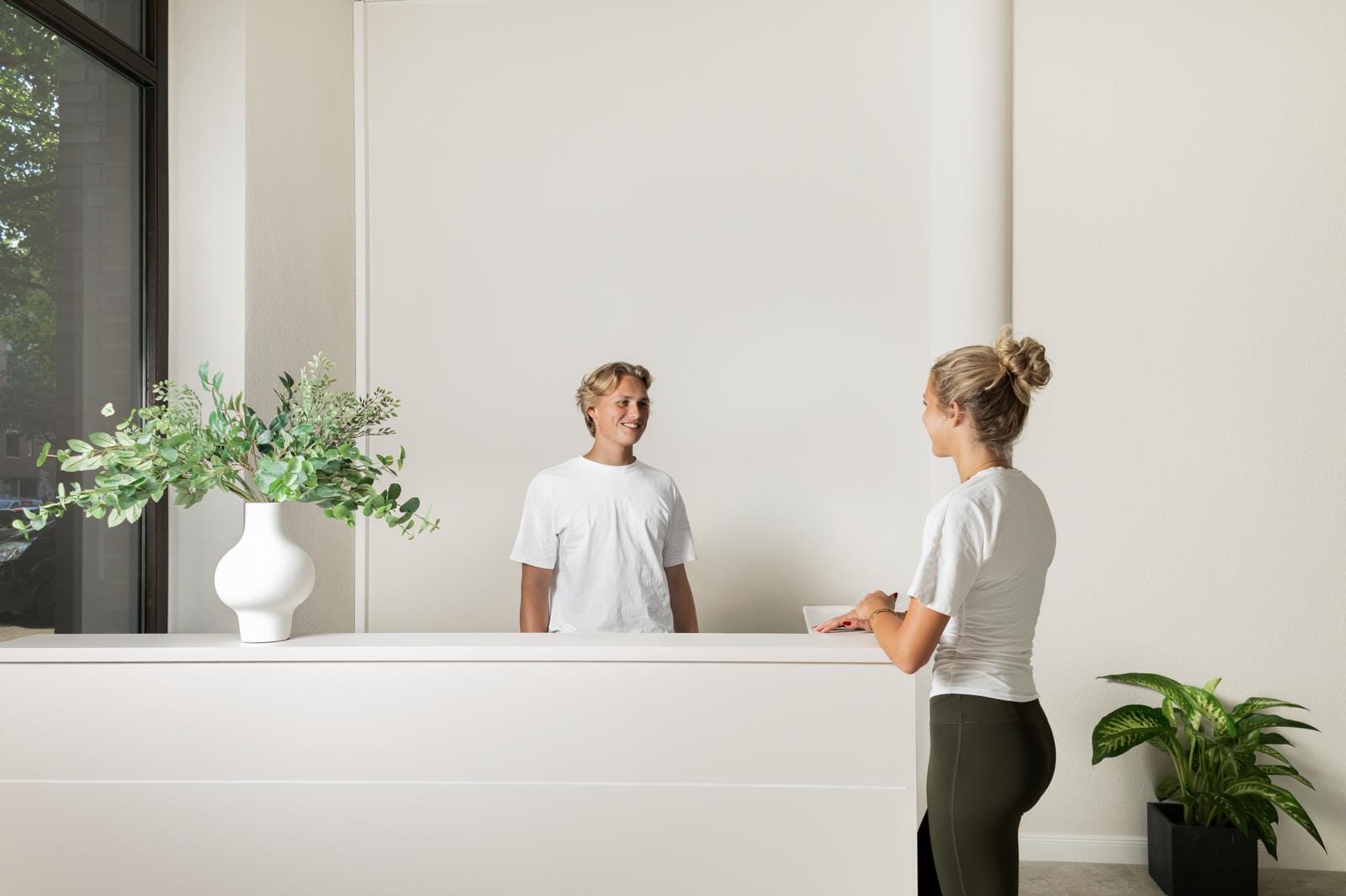 Heller Empfangsbereich der Praxis, ein Mitarbeiter begrüßt eine Patientin am Tresen