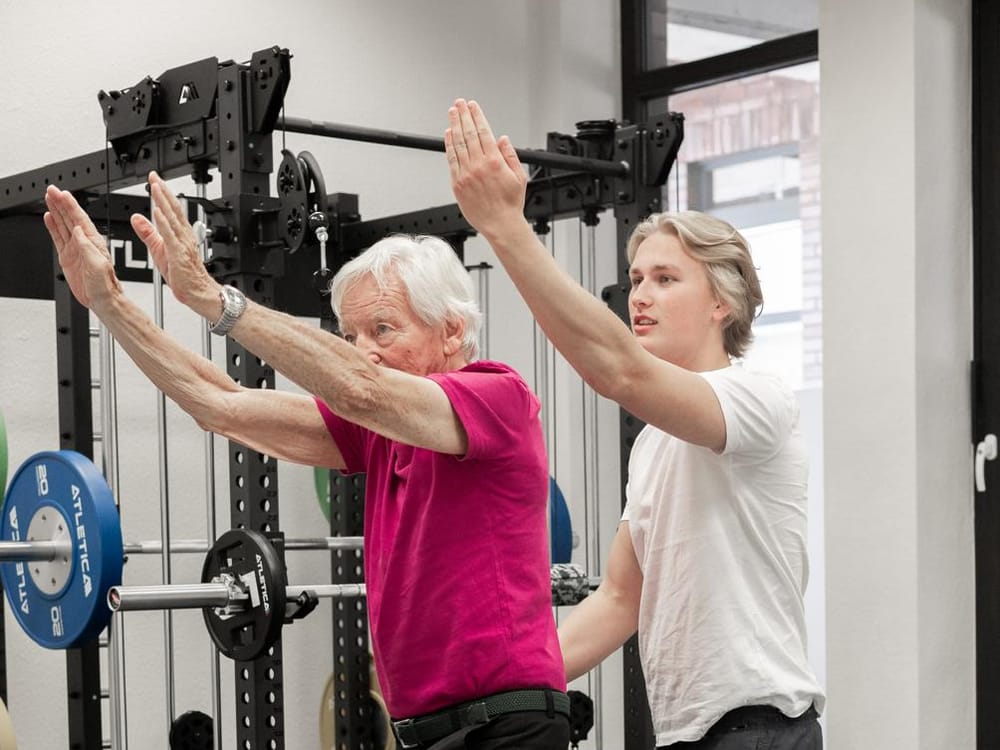 Therapeut begleitet einen älteren Patienten bei einer Gleichgewichtsübung auf dem Balance-Trainer